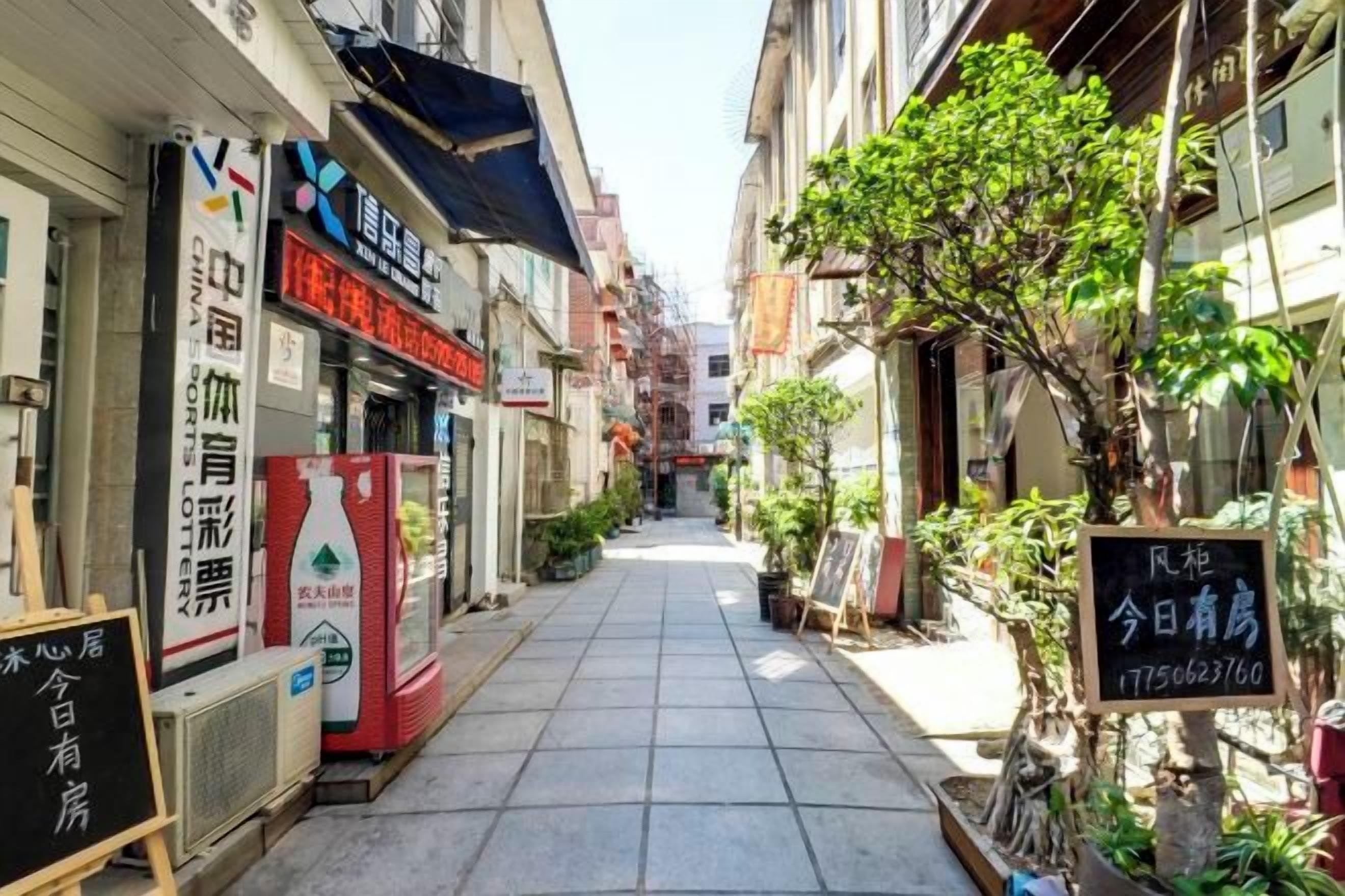 Un carrer estret amb edificis a ambdós costats, una placa amb text i un arbre.