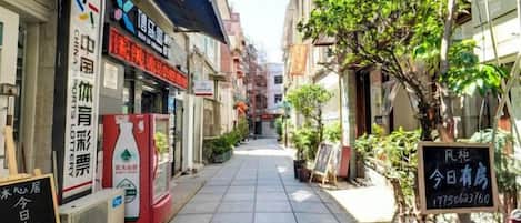 A narrow street with buildings on either side, a signboard with text, and a tree.