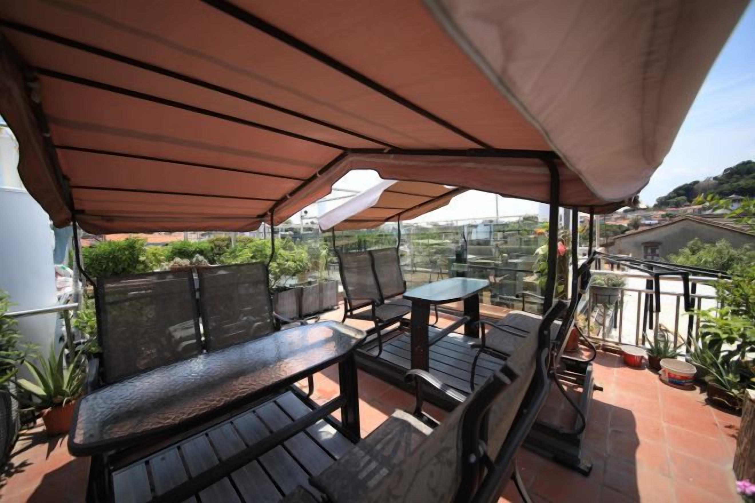 Une terrasse extérieure dotée d’un espace salon abrité, d’une table et de plantes en pot.