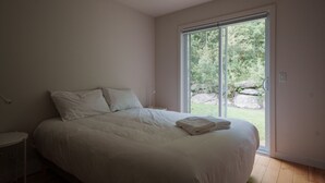 A bedroom with a large bed, a nightstand, and a sliding glass door leading to a garden.