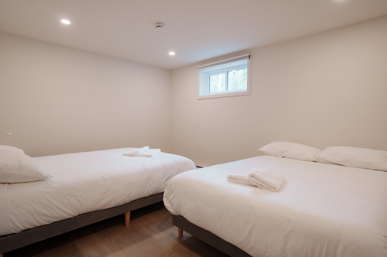 Two single beds with white linens and towels, a small window with blinds, and a recessed ceiling light.
