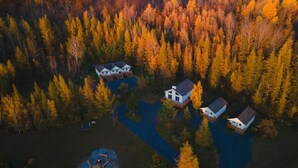Vue aérienne d’un quartier résidentiel avec trois maisons et un petit lac.