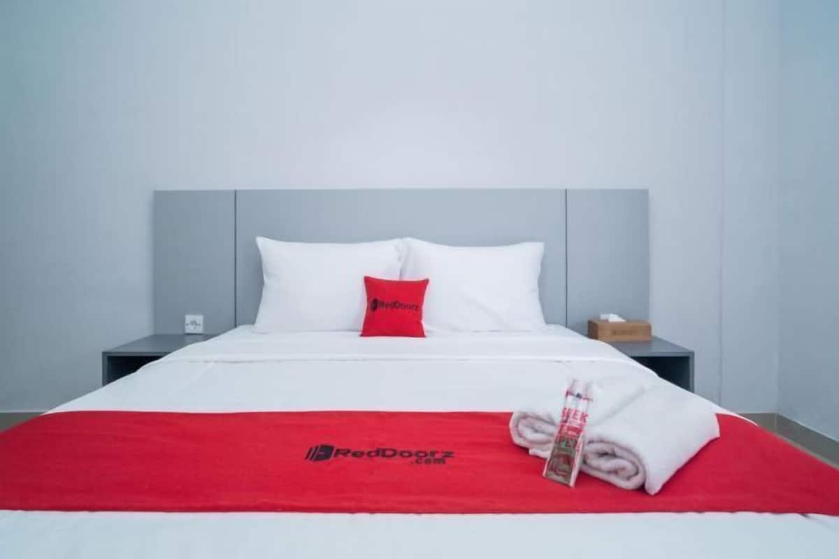 A hotel room with a bed, a red blanket, a white pillow, and a nightstand with a tissue box.