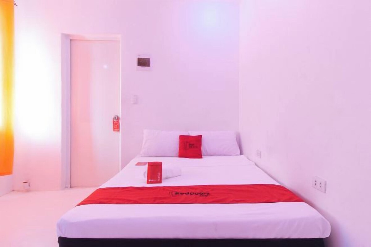 A hotel room with a bed, a red blanket, and a white wall.