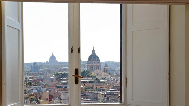 A view from a room with a large window, featuring a cityscape with prominent domed buildings. - Spanish Steps apartment with view by Flatinrome (ROMA)