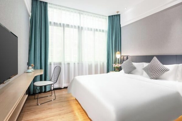 A hotel room with a bed, a desk, a chair, and a window with curtains.