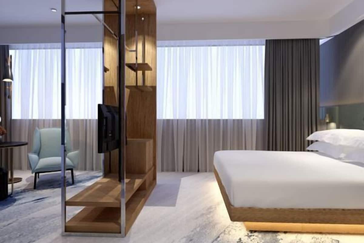 Une chambre d’hôtel moderne dotée d’un grand lit, d’un coin salon avec un fauteuil, d’une télévision et d’une structure en bois avec des étagères.
