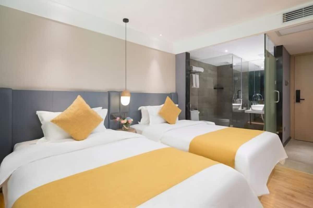 Une chambre d’hôtel avec deux lits, une douche à parois de verre et une salle de bain ouverte.