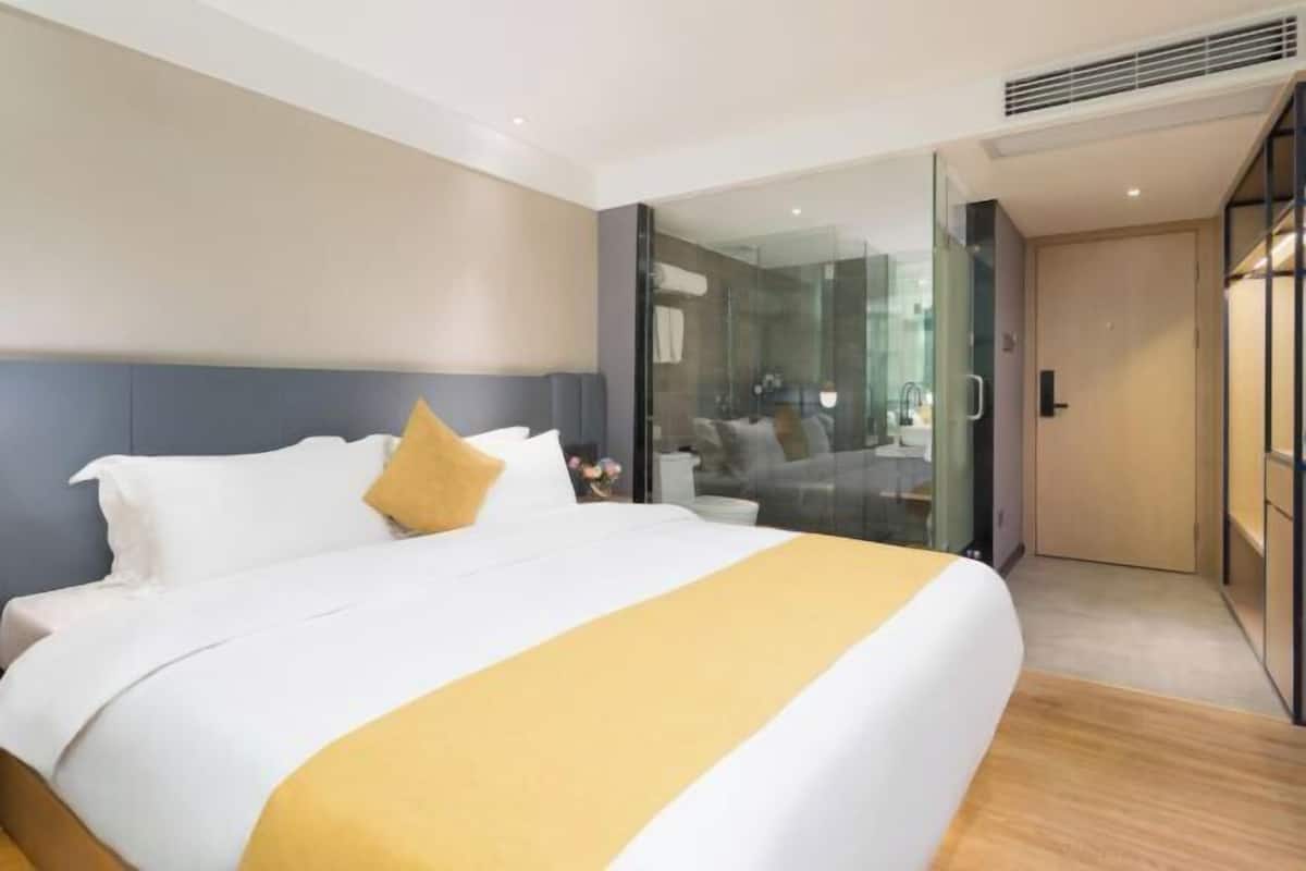 Une chambre d’hôtel moderne avec un grand lit, une cloison en verre et une vue sur la salle de bain.