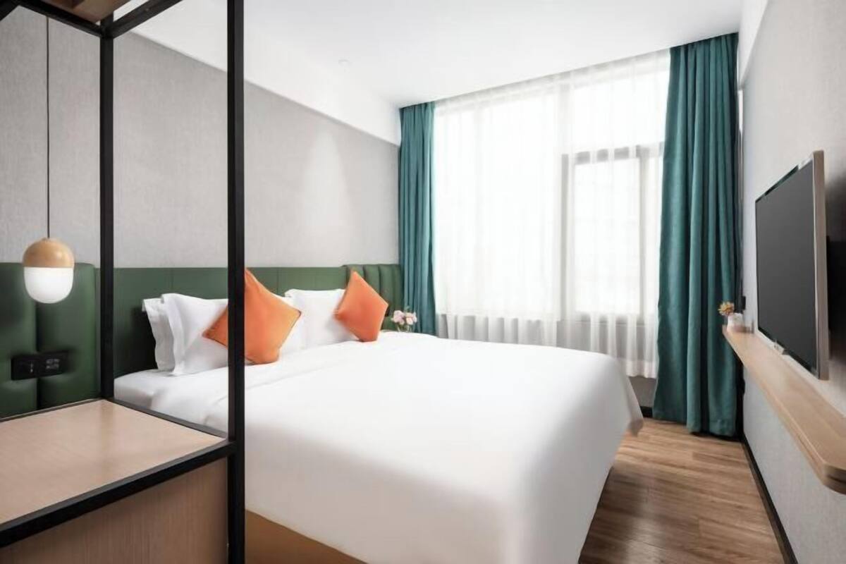 Une chambre d’hôtel avec un lit, une télévision, un bureau et une fenêtre avec des rideaux.