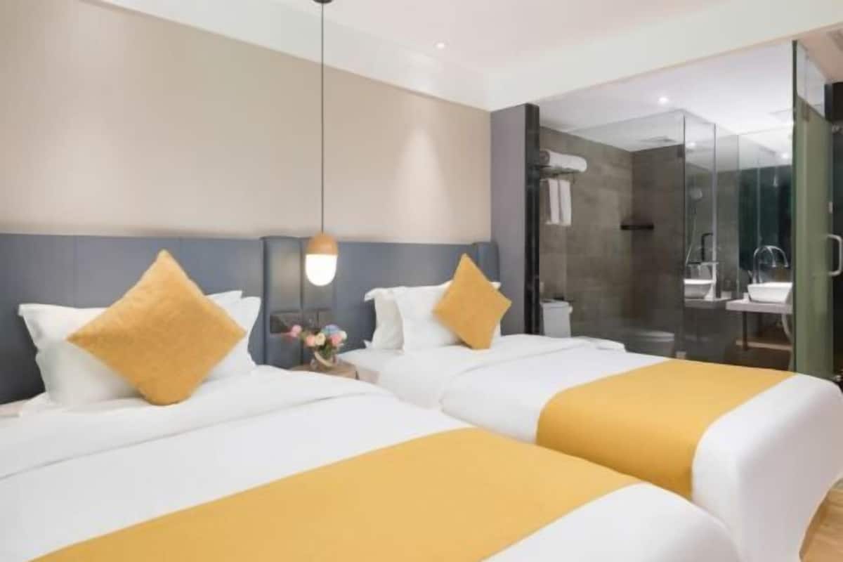 Une chambre d’hôtel avec deux lits, une table de chevet, une lampe et une cabine de douche en verre.