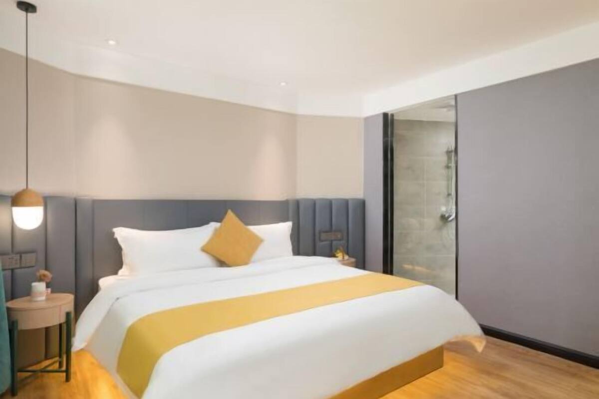 Une chambre d’hôtel moderne avec un grand lit, une table de chevet, une lampe et une douche en verre.