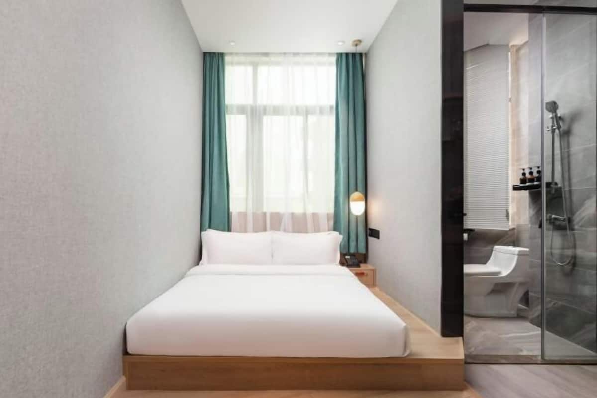 Une chambre d’hôtel moderne équipée d’un lit, d’une table de chevet, d’une cabine de douche en verre et offrant une vue sur la salle de bain.