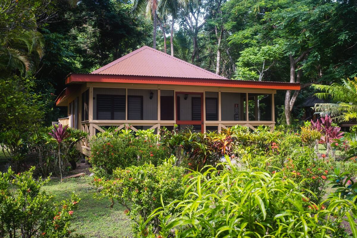Ein Haus mit rotem Dach, umgeben von üppiger Vegetation und unterschiedlichen Pflanzen.