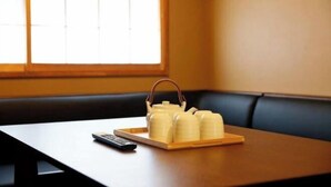 A wooden table with a tray holding several white bottles, a remote control, and a window with blinds in the background. - Kyokoi Toujimikuni (Kyoto)