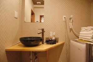 A bathroom with a wooden vanity, a large bowl sink, a mirror, a towel rack, and a white towel dispenser. - Kyokoi Toujimikuni (Kyoto)