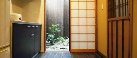 A narrow hallway with a sliding door leading to a small outdoor area, a black cabinet, and a traditional Japanese sliding door.