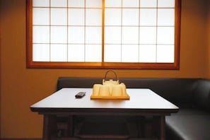 A table with a tray of folded towels and a remote control, a window with a grid pattern, and a dark-colored sofa. - Kyokoi Toujimikuni (Kyoto)