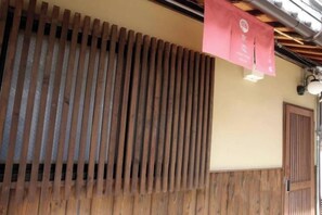 A building facade with a wooden slat design, a door, and a hanging sign. - Kyokoi Toujimikuni (Kyoto)