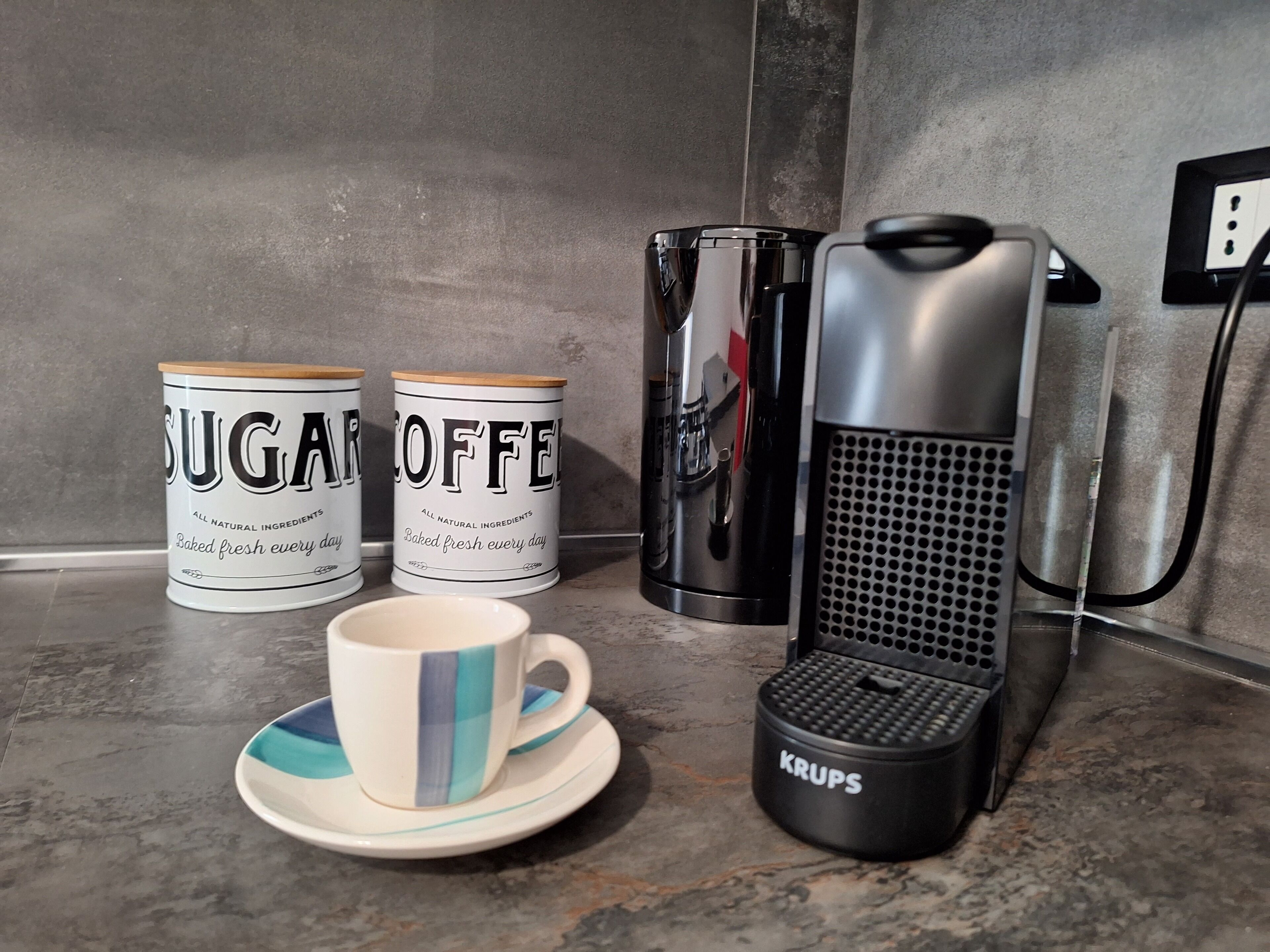 A kitchen counter with two sugar and coffee containers, a coffee machine, and a Krups electric kettle.