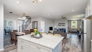 A spacious kitchen with a large island, a dining area with chairs, a staircase, and a living room with a sofa and a TV. - 5BR/5BA Arlington Getaway w/ Private Hot Tub Close to UTA & AT&T (Arlington)