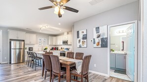 A modern kitchen with white cabinets, a stainless steel refrigerator, and a dining area with a wooden table and chairs. - 5BR/5BA Arlington Getaway w/ Private Hot Tub Close to UTA & AT&T (Arlington)