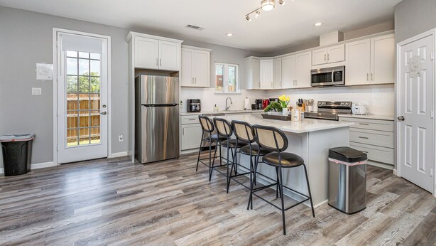 A modern kitchen with white cabinets, stainless steel appliances, and a central island with bar stools. - 5BR/5BA Arlington Getaway w/ Private Hot Tub Close to UTA & AT&T (Arlington)