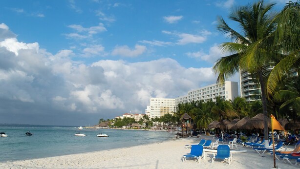 Ein Strand mit weißem Sand, klarem, blauem Wasser und einem Hotel im Hintergrund.