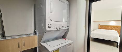 Een compacte hotelkamer met een wasmachine, een klein kastje en een bed met houten hoofdeinde.
