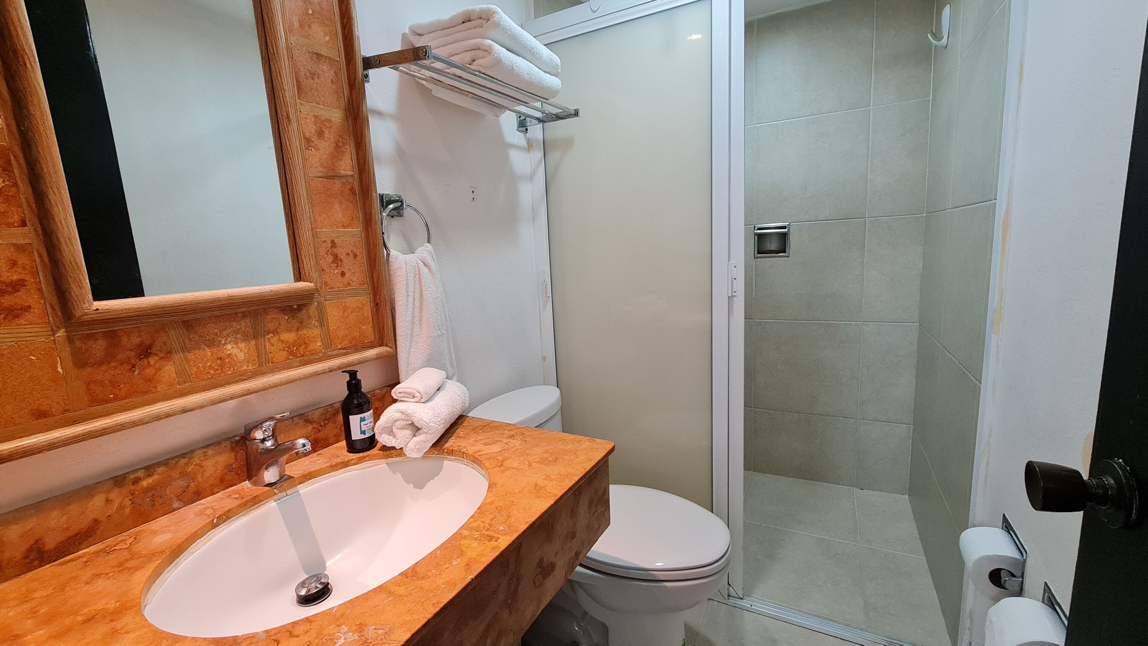 A bathroom with a marble sink, a toilet, a shower with glass doors, and a towel rack with folded towels.