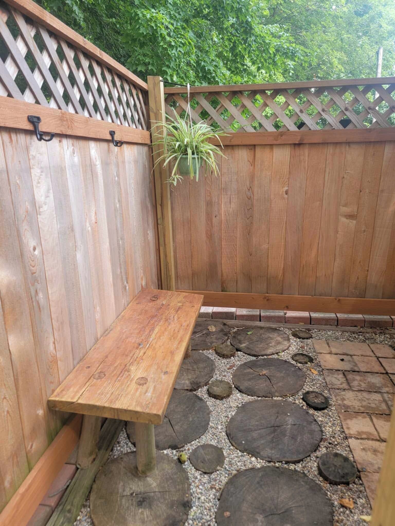 Una panchina di legno in un giardino con recinzione in legno e una pianta in vaso.