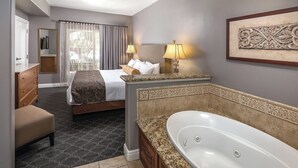 A hotel room with a bed, a sitting area with a chair, a large bathtub, and a mirror.