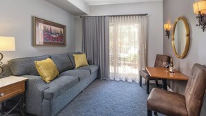 A hotel room with a grey sofa, a wooden table with a wine glass, a brown chair, a large mirror, and a painting on the wall. - Napa Valley | Napa Wine Getaway | Pool & Hot Tub (Napa)