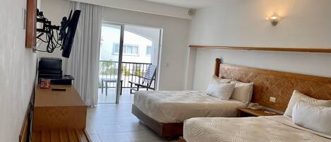 A hotel room with two beds, a desk with a computer, a chair, and a balcony with a view.