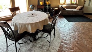 Een gezellige kamer met een houten plafond, een ronde tafel met stoelen, een bank en een open haard met planten.