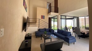 A spacious living area with a modern staircase, a dining area with outdoor seating, and large windows providing views of the outdoors. - VILLA GRACE tu mejor opcion en Cholul (Mérida)