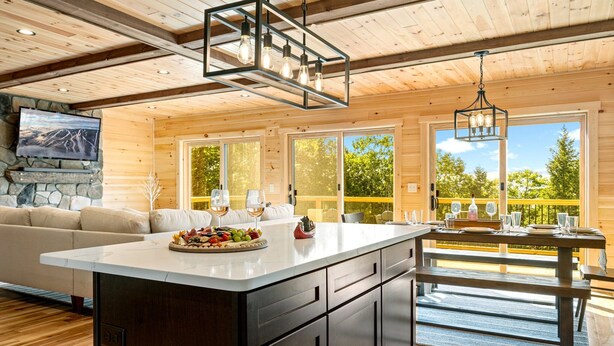 A spacious kitchen with a large island, wooden cabinets, and a stone fireplace. - Secluded Cabin with Hot Tub, Views, & EV Charger (Bryant Pond)
