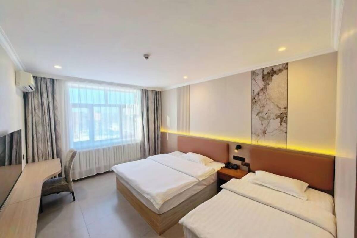 Habitación de hotel con dos camas, un escritorio y un ventanal grande con cortinas.