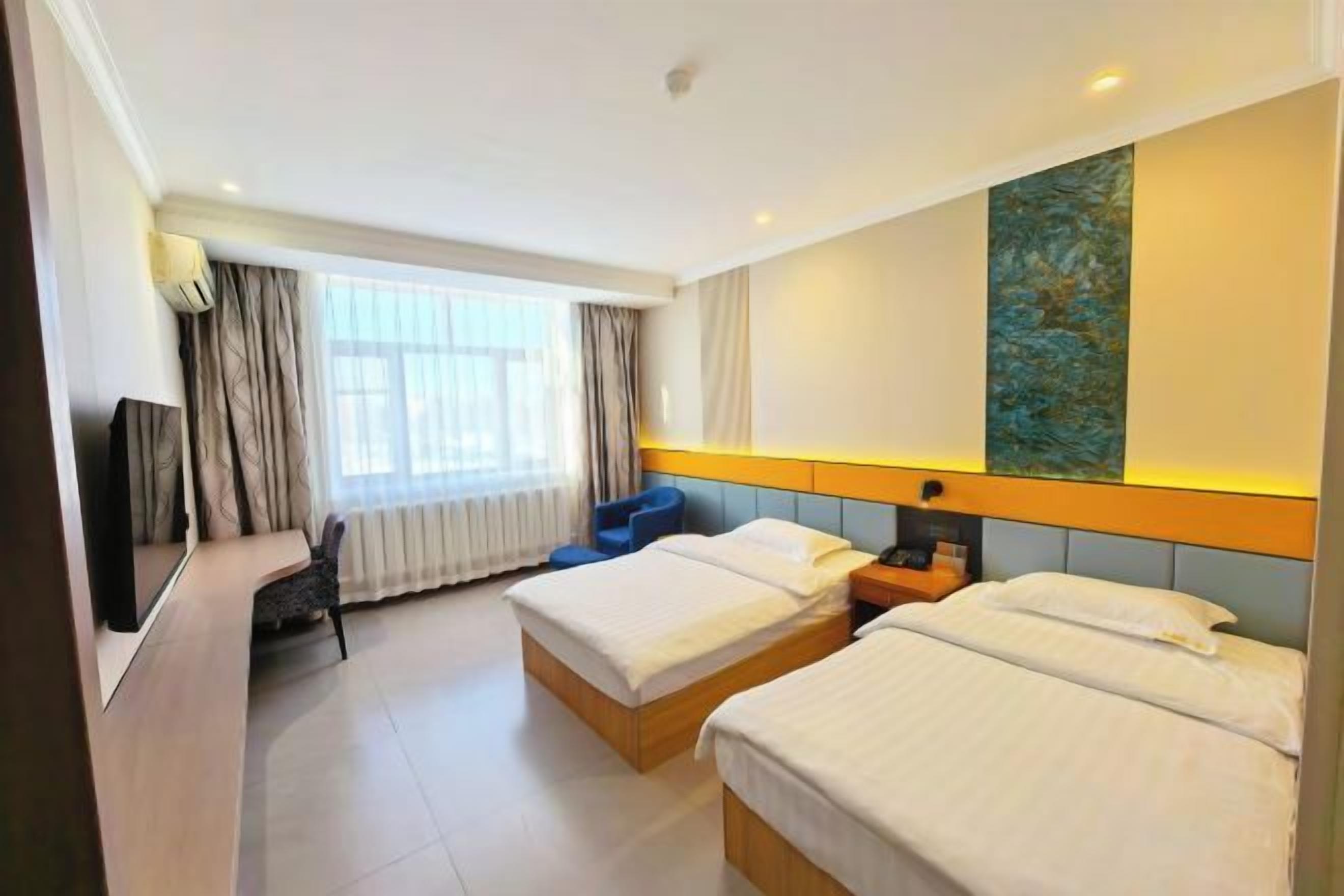 A hotel room with two beds, a desk, a chair, a TV, and a large window with curtains.