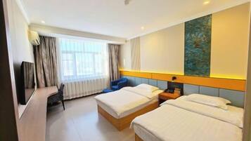 A hotel room with two beds, a desk, a chair, a TV, and a large window with curtains.
