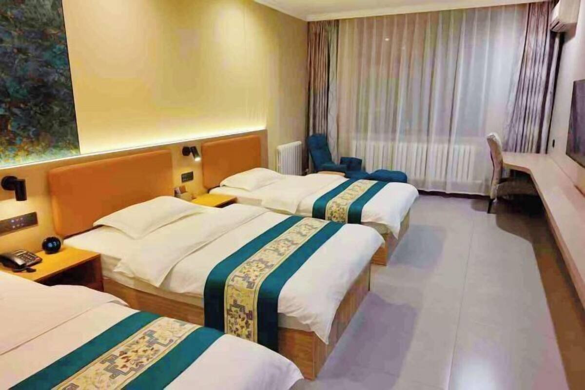 Habitación de hotel con tres camas, un escritorio, una silla y un amplio ventanal con cortinas.