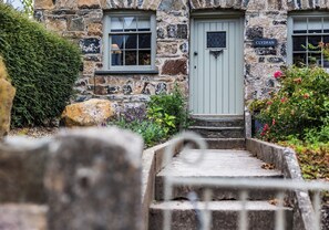 Clydfan's traditional stone building offers a charming entrance with a light green door and two windows.