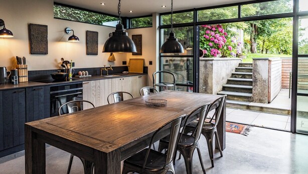 A modern kitchen with a wooden dining table and chairs, a large window with a view of greenery, and pendant lighting. - A character cottage with a contemporary glass extension, in the heart of Newport (Newport)