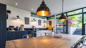 A modern kitchen with dark cabinetry, a wooden dining table, and pendant lighting. - A character cottage with a contemporary glass extension, in the heart of Newport (Newport)