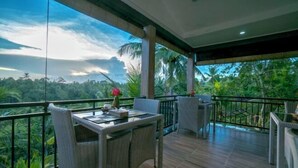A balcony with wicker furniture and a table, overlooking a lush green landscape. - Adi Bisma Inn by Mahaputra (Bali)