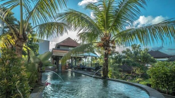 A pool area with palm trees, a fountain, and a covered seating area. - Adi Bisma Inn by Mahaputra (Bali)