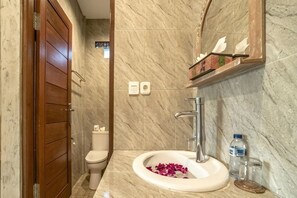 Ein Badezimmer mit Marmorwaschbecken, einer Holztür, einer Toilette und einem Ablagefach mit Pflegeprodukten.