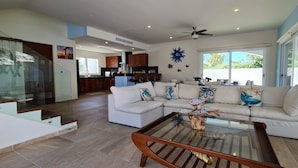 A spacious living room with a glass coffee table, a white sectional sofa, and a kitchen in the background. - CASA REYES Stunning Rooftop Oceanview (Isla Mujeres)