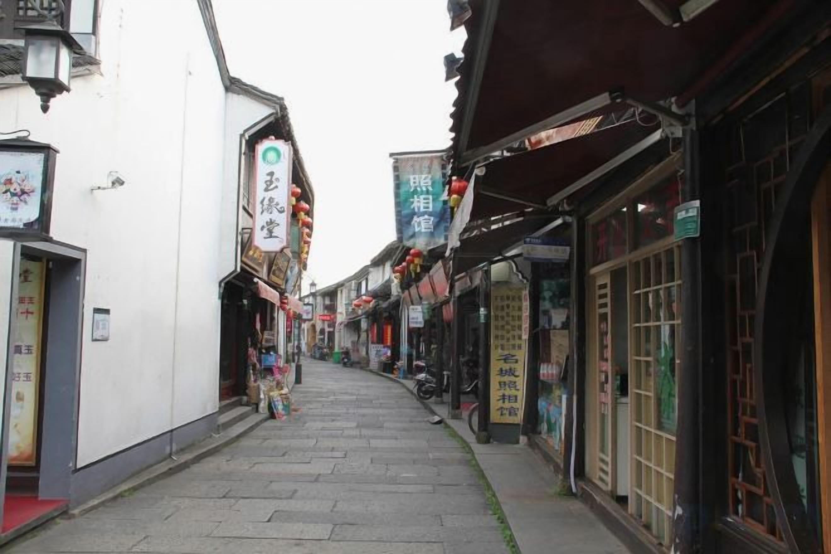 A narrow street with traditional architecture, shops, and signage.