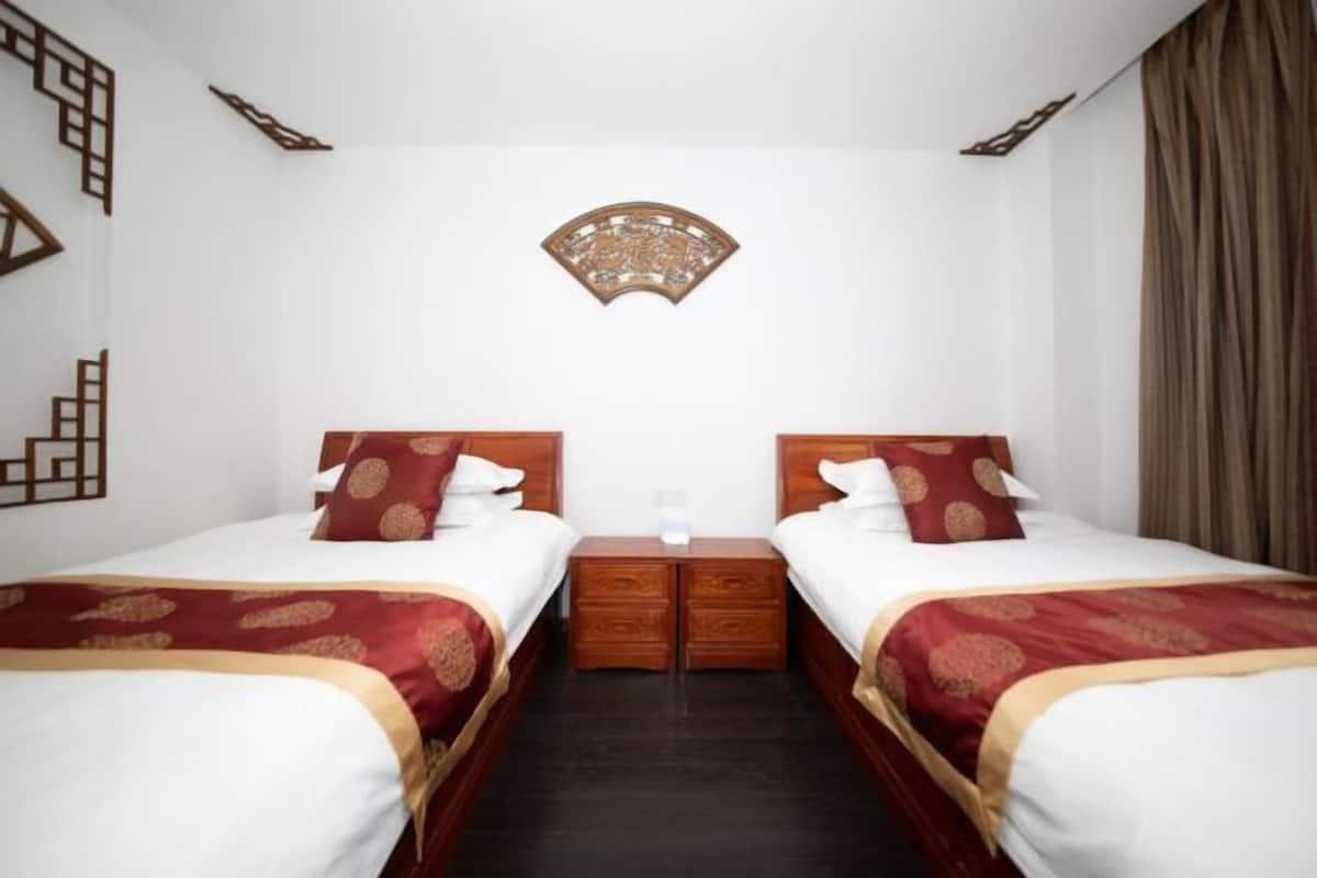 Ein Hotelzimmer mit zwei Betten, einem hölzernen Nachttisch dazwischen und einem dekorativen Wandbild darüber.